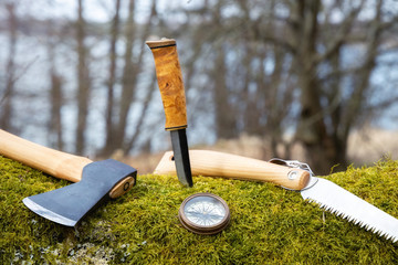 Travel equipment for a forest trip . Axe, knife, compass and saw on the moos. Survival kit. Adventure concept.