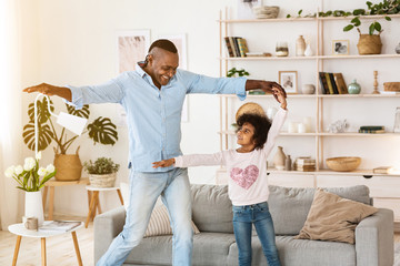 Stay at home leisure. Senior African American man dancing with his granddaughter indoors