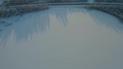 Aerial drone shot of a frozen lake, blocks of ice, frozen trees, reflections, typical house during the winter of polar Lapland.