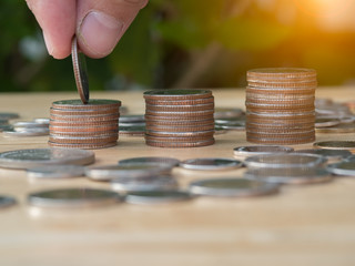 Saving money hand putting coins on stack on table with sunshine on nature background