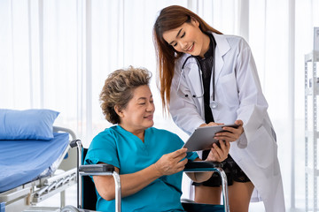 Asian medical doctor take care and explain senior elderly woman female patient on wheelchair with tablet