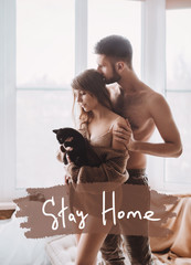 Stock photo - I stay at home awareness social media campaign and coronavirus prevention. Stay home phrase. Happy loving couple  play with her kitten at home