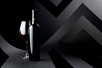 Bottle and glass of red wine on a dark background.