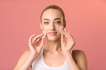 Girl using cotton pads looking at camera on pink background