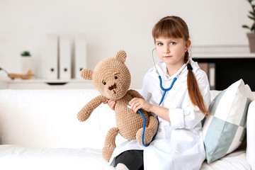 Sticker - Cute little doctor playing with teddy bear in clinic