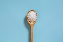 Coarse Sea Salt In A Wooden Spoon On A Blue Background. Ingredient For Cooking And Spa Treatments.