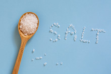 Coarse Sea Salt In A Wooden Spoon On A Blue Background. Ingredient For Cooking And Spa Treatments. The Inscription "salt".