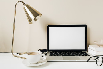 blank screen laptop. home office desk table workspace with coffee, lamp, glasses, notebook on beige 