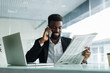 © dianagrytsku - African american man reading newspaper and talking on phone in office