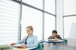 © Seventyfour - Wide angle portrait of blonde intelligent girl reading book while sitting at desk in school classroom, copy space