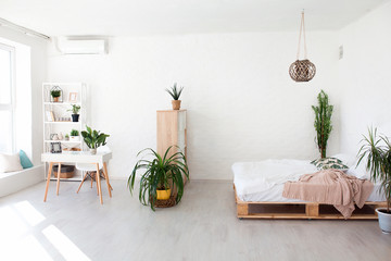 Cozy bedroom area at luxury studio apartment with a free layout in a loft style with big panoramic window and green plant.