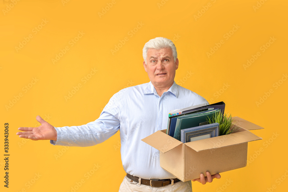 Sad fired mature man with personal stuff on color background