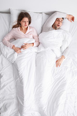 Wall Mural - Young irritated woman in bed with snoring husband at home