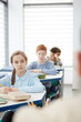 © Seventyfour - Multi-ethnic group of children sitting in row at desk in school classroom and listening to teacher, copy space