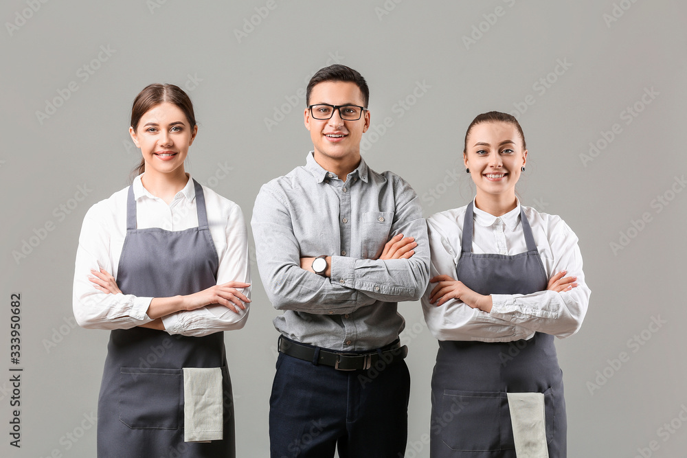Young waiters with teacher on grey background
