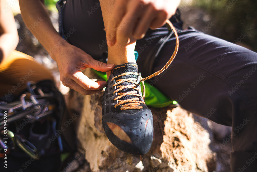 Rock climber puts on climbing shoes and ties shoelaces. - obrazy, fototapety, plakaty 