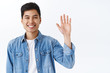 Close-up portrait of friendly attractive asian man waving to say hi, informal greeting gesture, laughing and smiling as welcoming new members join team, hello sign, white background