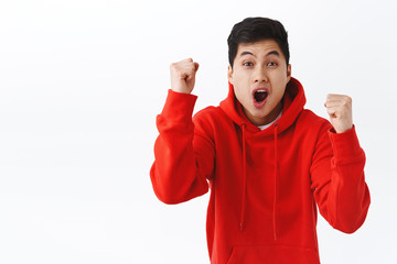 Wall Mural - Waist-up portrait of excited happy asian man likes sport games, rooting for team, raising hands up in triumph, celebrating victory or success, chanting scored goal, standing white background