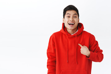 Wall Mural - Portrait of excited, happy smiling man in red hoodie pointing at himself as being chosen or picked, achieve goal, talking personal goal, standing cheerful white background