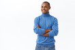 © Cookie Studio - Portrait of dreamy, successful young african american businessman in blue turtleneck, cross hands over chest, look away left side copy space, wtih satisfied, pleased expression, white background