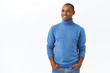 © Cookie Studio - Business, investmenent and profit concept. Portrait of pleased, happy young elegant african-american male entrepreneur in blue turtleneck, hold hands in pockets, looking left with satisfied smile