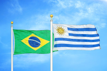 Brazil and Uruguay two flags on flagpoles and blue cloudy sky