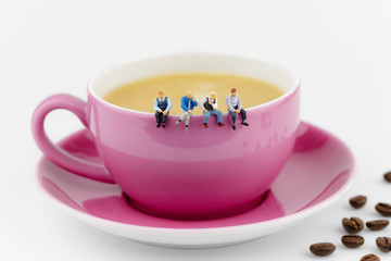 miniature men sitting on a pink cup of coffee isolated on white background and coffee beans