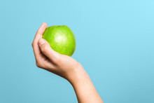 Close Up Woman Hand Holding Green Apple Against Blue Background. Choosing Healthy Lifestyle