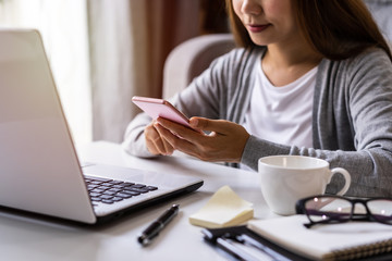 Young woman sitting at living room and working on laptop and smartphone at home