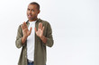 © Cookie Studio - No thank you, I pass. Portrait of young african-american man rejecting persons offer, raising hand in block, rejection, step away from friend coughing, staying at home during quarantine