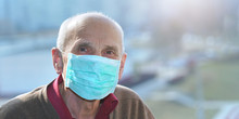 Old Man In Protective Face Mask Anti Virus Looks In Camera Window Background
