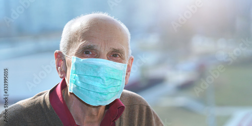 old man in protective face mask anti virus looks in camera window background