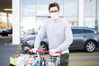 Mann mit vollem Einkaufswagen vor einem Supermarkt, Atemmaske und Handschuhe als Schutzmaßnahme