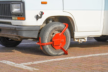 Parking Wheel Lock. Clamped Front Wheel Of Illegally Parked Car, Red Clamp Attached To Wheel. Car Parked Illegally Is Fined And Wheel-locked By The Police.