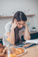 Girl reading cookbook at the kitchen, looking for recipe. Confusion emotion