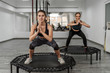 Portrait of two young active girls in fitness clothes doing exercises for  squatting with trampoline during training in gym