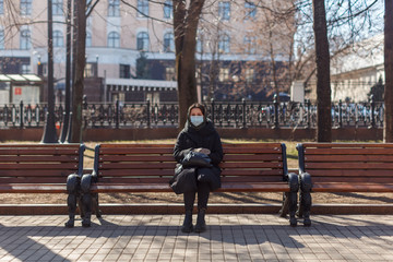 lonely woman with medical mask alone in park sitting on bench at sunny day