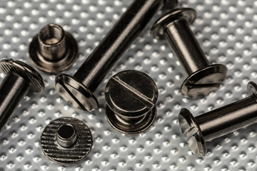 A Macro image of various sized Chicago Screws or Barrel Bolts of varying lengths on a stainless steel industrial background.