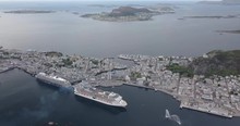 High Altitude Aerial Footage Of Two Luxurious Cruise Ships Docking At The Port Of Alesund, The Most Beautiful Town In Norway, While A Tugboat Performs A Water Salute By Spraying Water In The Air.