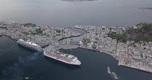 High Altitude Drone Footage Of Two Luxurious Cruise Ships Docking At The Port Of Alesund, The Most Beautiful Town In Norway, While A Tugboat Performs A Water Salute By Spraying Water In The Air.