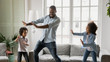 © fizkes - Happy African ethnicity father have fun teaches little preschool kids to dance in modern living room at home. Dad with son and daughter engaged in funny activity enjoy leisure carefree weekend concept