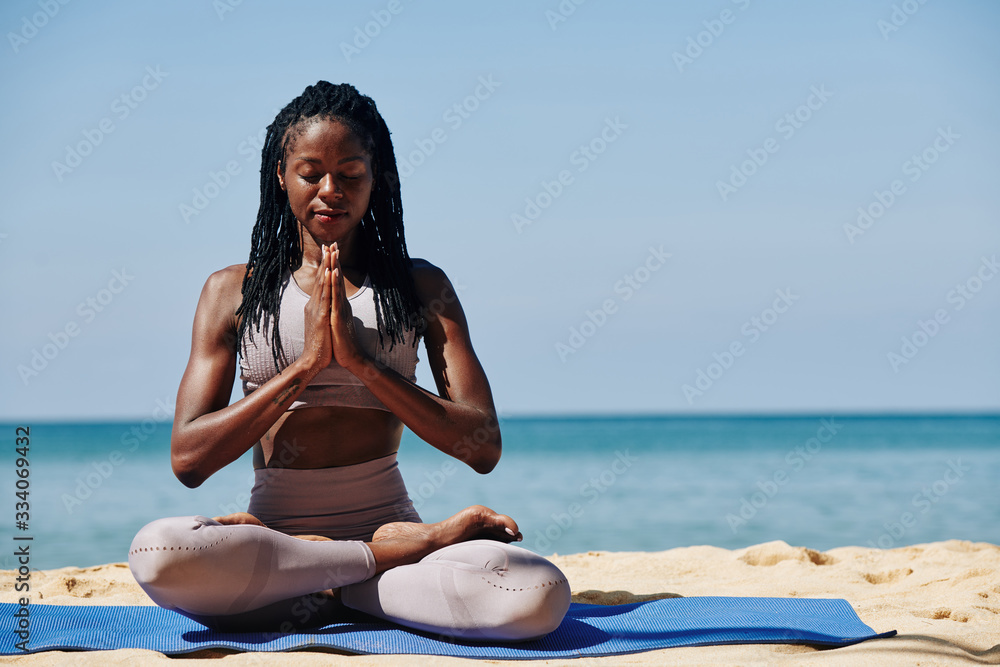 Beautiful slim young woman meditating in lotus position on the beach - obrazy, fototapety, plakaty 