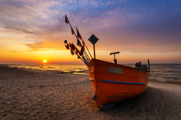 Wall Mural - colorful fishing boat on a sandy sea beach during a beautiful sunset