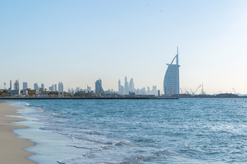 Wall Mural - Burj Al Arab in Jumeirah Island or boat building with waves on sea beach, Dubai Downtown skyline, United Arab Emirates or UAE. Financial district in urban city. Skyscrapers at sunset.