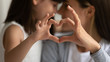 © fizkes - Close up of young mother and cute little daughter make heart sign with hands enjoy close tender moment together, caring mom and grateful small girl child show love and support in family relationships