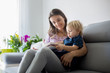 © Tomsickova - Young woman, mother with three kids, reading a book at home, hugging and laughing