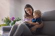 © Tomsickova - Young woman, mother with three kids, reading a book at home, hugging and laughing