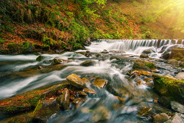 Wall Mural - Waterfall on mountain river in autumn forest under bright sun