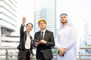 A business meeting with an arab man and his assistance or a translator, discussing planning business on a smart tablet device and a clipboard documentation within the urban city district background..