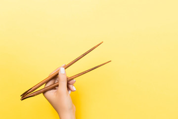 Wall Mural - Female hand with chopsticks on yellow background. Traditional asian food with emty space for your design